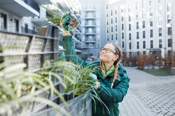 Junge Auszubildende im Gartenbau greift nach einem Blumentopf
