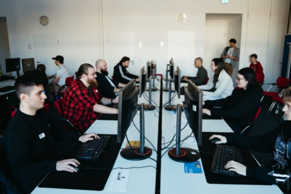 Mehrere Männer sitzen sich in einem Raum des Helmholtz Zentrums gegenüber und spielen Computerspiele. Ihr Gesichtsausdruck ist fröhlich.