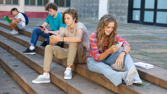 Jugendliche sitzen auf einer Treppe und blicken auf ihre Smartphones.