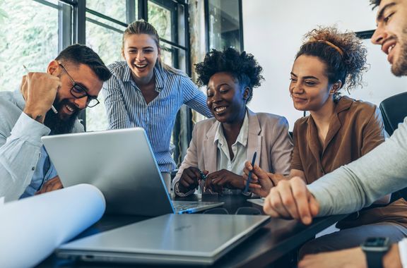 Tausendsassa-Potenzial gewinnen und halten Ein Team von jungen Menschen sitzt vor einem Notebook und freut sich über gemeinsamen Erfolg