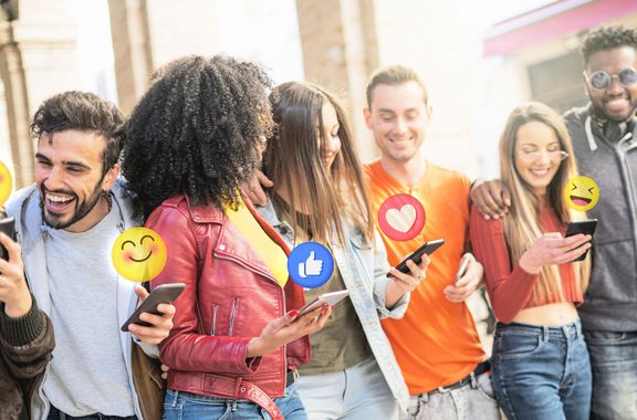 5 Gründe warum Social Media Ihre Zukunft beeinflusst Sechs junge Menschen mit gemischtem ethnischem Hintergrund lachen und haben Handys in der Hand