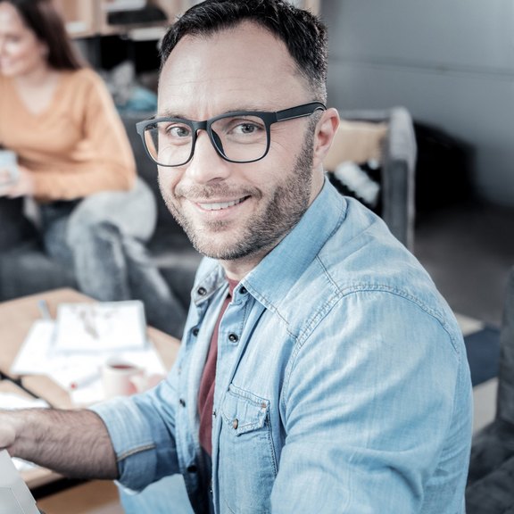 Mann in Hemd am Laptop sitzend der in die Kamera schaut