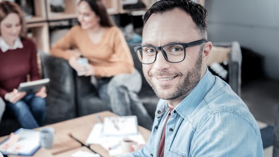Mann in Hemd am Laptop sitzend der in die Kamera schaut