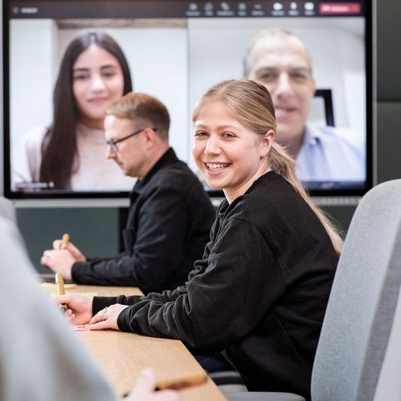 mehrere Personen mit einem Online-Meeting im Hintergrund