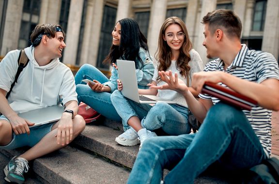 Interne Kommunikation in der Ausbildung 4 junge Menschen sitzen auf einer Treppe und reden miteinander