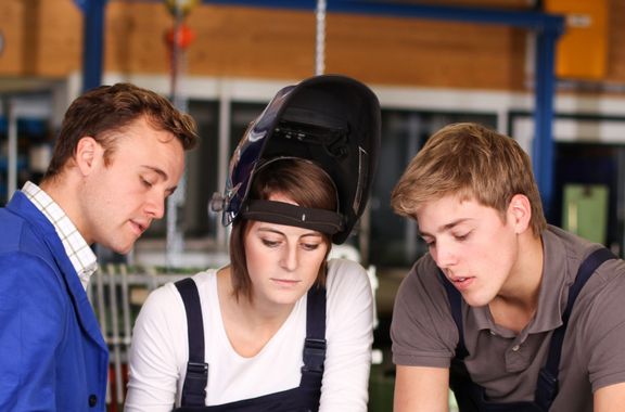 Ein Ausbilder schult eine weibliche und einen männlichen Azubis an der Werkbank