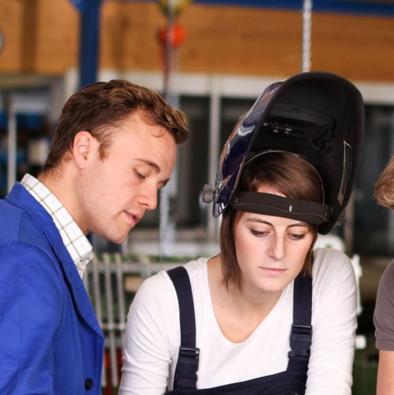 Ein Ausbilder schult eine weibliche und einen männlichen Azubis an der Werkbank