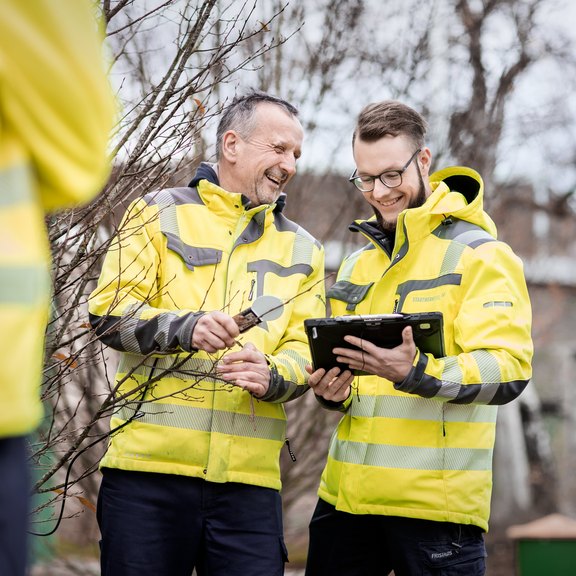 Zwei Männer, in gelber Arbeitskleidung, schauen gemeinsam auf ein Tablet.