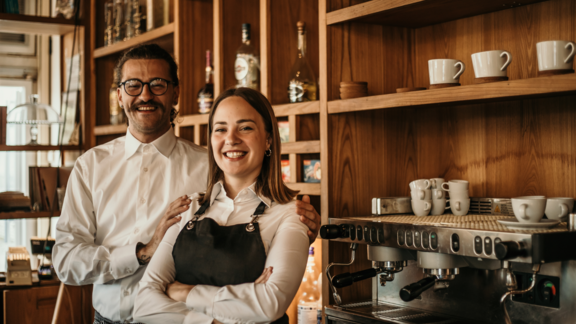 Zwei Café-Mitarbeitende lächeln stolz hinter der Theke.