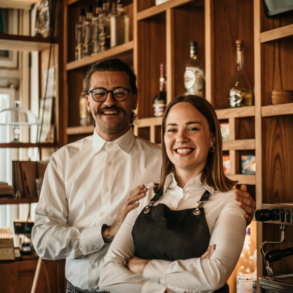 Zwei Café-Mitarbeitende lächeln stolz hinter der Theke.
